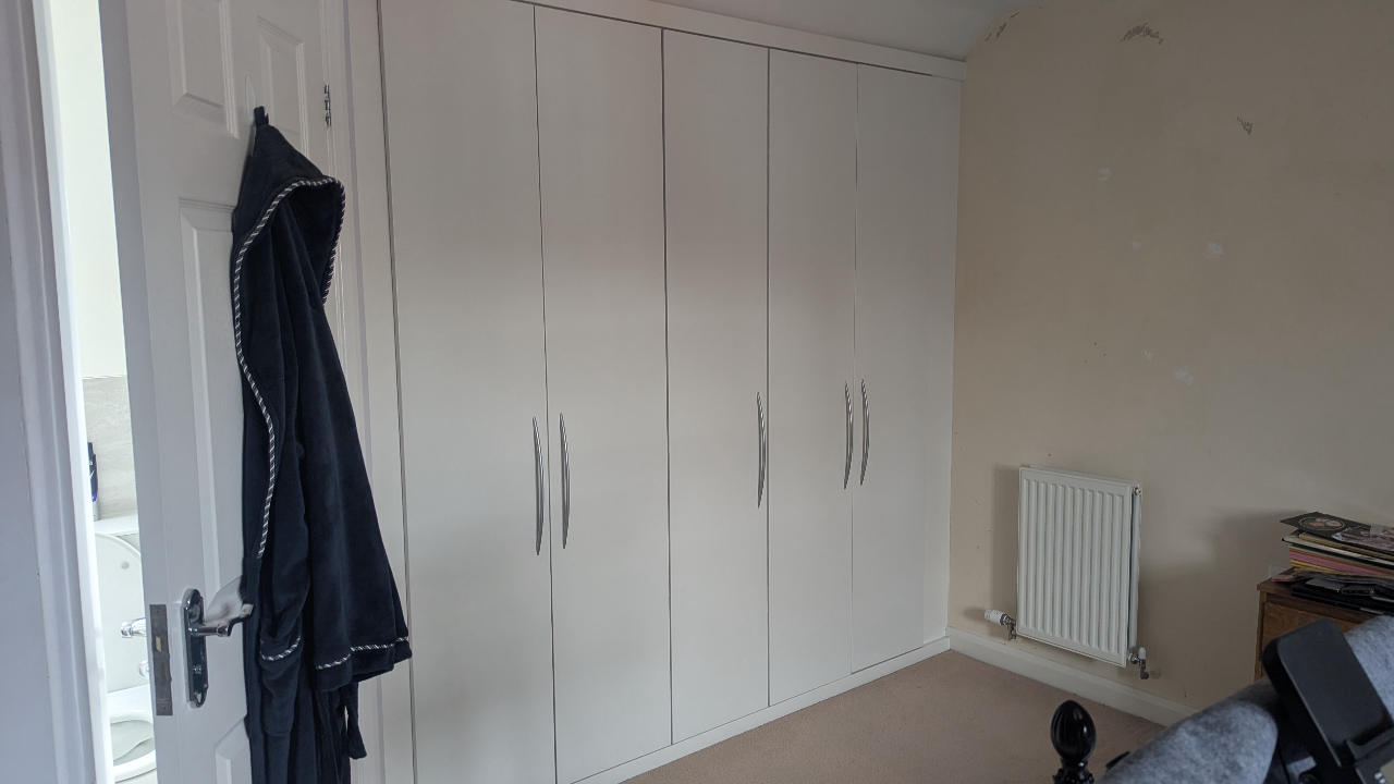 Wall-to-wall white fitted wardrobes in a bedroom before removal